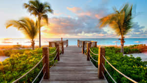 A Wooden Walkway Leading To The Beach At Sunset Wallpaper