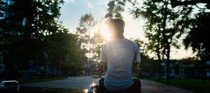 A Young Boy Walking Down A Road At Sunset. Wallpaper