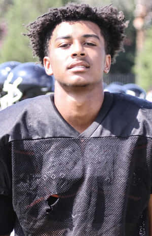 A Young Man In A Football Uniform Standing On The Field Wallpaper