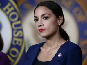 Alexandria Ocasio-cortez In Front Of Blue Backdrop Wallpaper