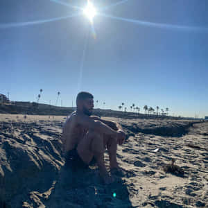 Amir Albazi Sitting On Sandy Beach Wallpaper