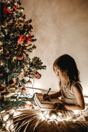 An Adorable Little Girl Sits In The Middle Of A Festive Array Of Twinkling Lights And Pine Branches Just In Time For Christmas. Wallpaper