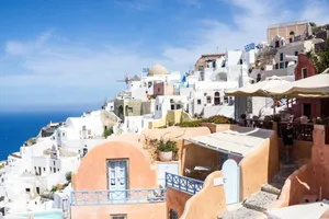 An Exquisite View Of Santorini's Iconic Blue-domed Churches And Whitewashed Houses Overlooking The Shimmering Aegean Sea. Wallpaper