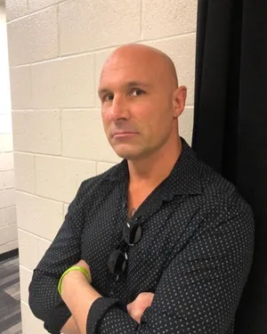 Bald Manin Black Shirt Leaning Against Wall Wallpaper