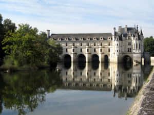 Breathtaking View Of Chenonceau Castle Amidst Riverside Vegetation Wallpaper