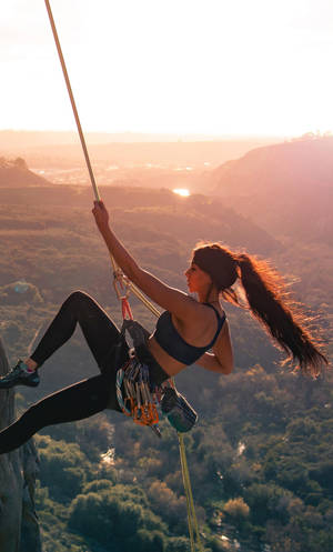 Caption: Fearless Female Rock Climber Ascending A Cliff Wallpaper