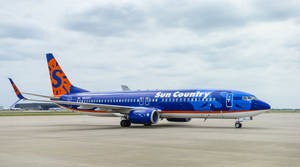 Cloudy Skies Over A Blue Aircraft Of Sun Country Wallpaper