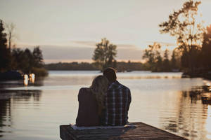 Couple Hugging On The Dock At Sunset Wallpaper