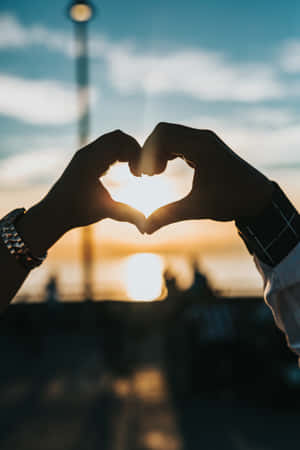 Couple Making A Heart Shape With Hands At Sunset Wallpaper