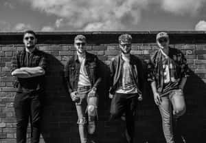 Four Young Men Standing In Front Of A Brick Wall Wallpaper