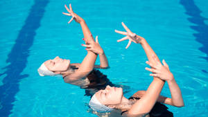 Graceful Artistic Swimmers Performing Synchronized Movements Wallpaper