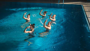 Group Performance In Artistic Swimming Showcasing Exquisite Coordination And Fluid Movements Wallpaper