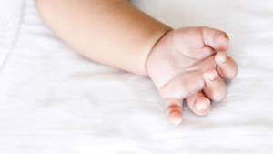 Innocence Cradled: Baby Hand Resting On A White Sheet Wallpaper