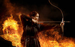 Katniss Everdeen From The Hunger Games Series Aiming With Bow Wallpaper