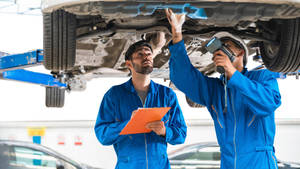 Proficient Mechanical Engineer Technician Inspecting A Car Wallpaper