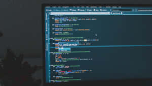 Programmer Writing Code At A Desk With Dual Monitors Wallpaper