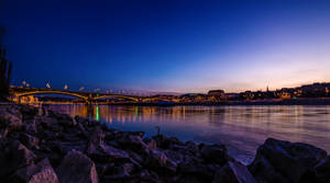 Rocky Riverside With View Of Bridge Wallpaper