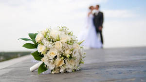 Romantic Couple Sharing A Kiss Behind A Vibrant Wedding Bouquet. Wallpaper