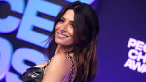 Sarah Shahi Smiling Against A Serene Background Wallpaper