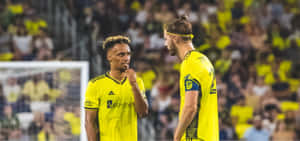 Soccer Players Discussing Strategy On Field Wallpaper