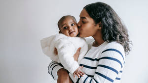 Tender Moment Of Love - Mother Planting A Kiss On Child's Cheek Wallpaper