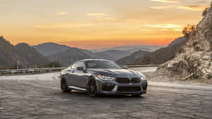 The Bmw M8 Is Driving Down A Mountain Road At Sunset Wallpaper