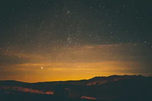 The Enchanting Night Sky Above The Hills Of A Village Wallpaper