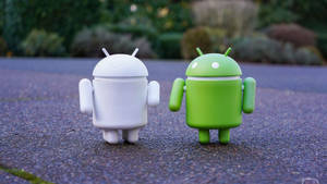 Two Android Toys Standing Next To Each Other Wallpaper