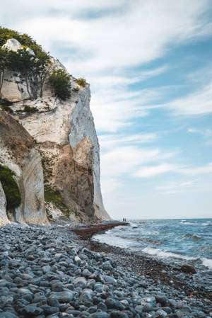 Two Person Standing Between Cliff And Body Of Water Wallpaper