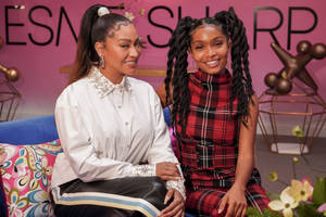 Two Women Sitting On A Couch With A Pink Background Wallpaper