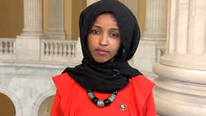 U.s. Representative Ilhan Omar Posing Elegantly In An Orange Dress Wallpaper