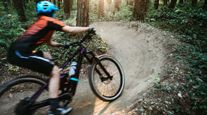 Woman Uphill Mountain Biking Adventure Wallpaper